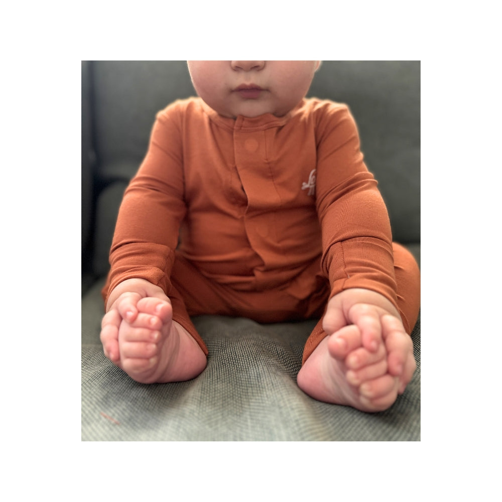 Baby wearing Birdie terracotta orange bamboo sleepsuit with magnetic closure and soft stretch